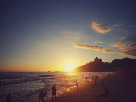 Sunset on a beautiful tropical beach, with people having fun. and silhouette of the mountains of Rio de Janeiro in a calm environmentの写真素材