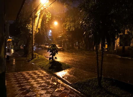 Dark street covered with water due to a torrential rain with reflections of faint yellow lights. Storm and mystery nightのeditorial素材