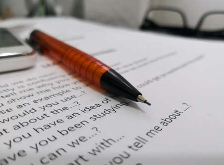 Orange pencil on a piece of paper with an English text that contains questions. Writing, study and reading concept.のeditorial素材