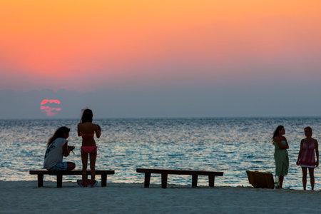 Young people are standing at the beach of a Maldives island at duskの写真素材