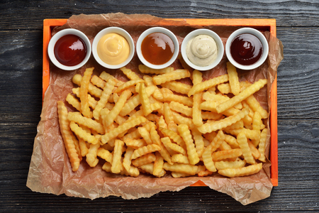 French fries on big wooden tray with sauces on black wooden backgroundの写真素材