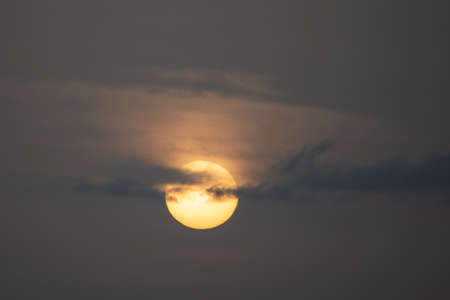 sunset with orange sun blocked by cloudsの写真素材