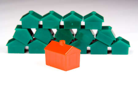 A little red plastic house in focus in the foreground, in front of a neat and orderly stack of similar green ones, in a blurry background.の写真素材