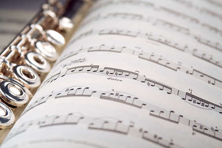 A used flute lies along the spine of an open musical score. Only one line of music is in focus.の写真素材