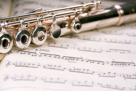 A used flute rests across an open musical score. Only one line of music is in focus.の写真素材