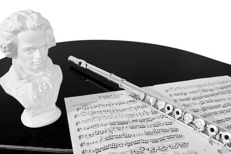 A flute, musical score and bust of Beethoven rest on a black piano top, isolated against a white background. Black and white (grayscale).の写真素材