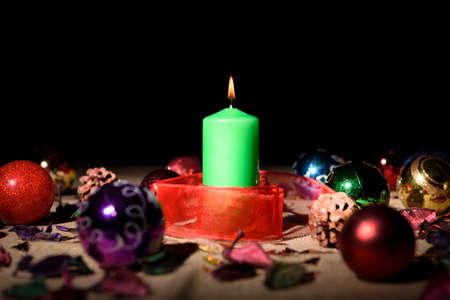 Green candle on table with decorations for Christmas tree around it on black background.の写真素材