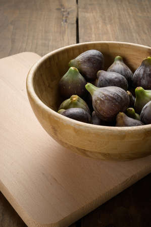 Top view of figs in wooden bowl on wooden table, vertical, with copy space