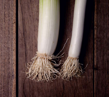 A leek on a rustic wooden table in a dark environment.