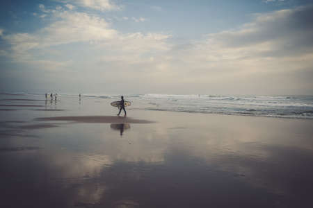 BOY SURFER AT SUNSET LEAVING THE SEA WIT YOUR SURFBOARTの写真素材