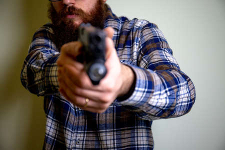 young man with plaid shirt holding a gun pointing at the cameraの写真素材