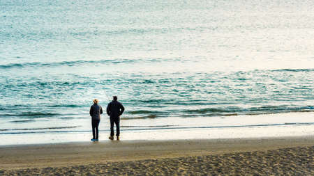 Two people standing on the beach with fishing polesの写真素材