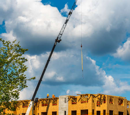 Construction workers on roof with crane and cumulus clouds in backgroundのeditorial素材