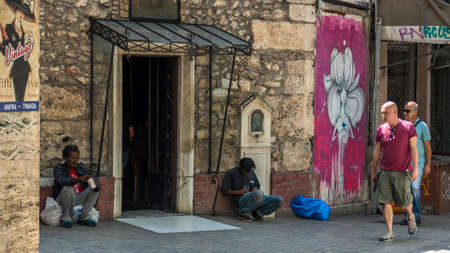 Athens Greece/August 17, 2018: Two homeless men sitting in front of chruch with people walking byのeditorial素材