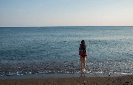 Teen standing at water's edge with towel looking out to seaの写真素材