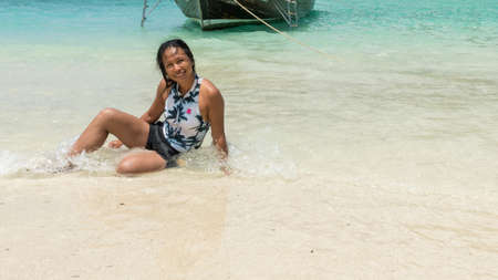 Asian woman sitting at edge of beach in water on tropical island