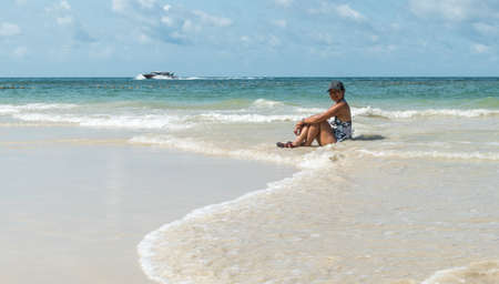 Woman sitting in water at beach in hat and one piece bathing suitの写真素材