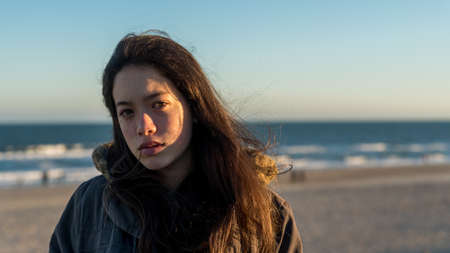 Young Asian-American at North Carolina Beach in winter in parka with sea in background