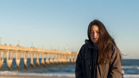 Young Asian-American at North Carolina Beach in winter in parka with fishing pier in backgroundの写真素材