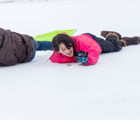 Young Asian girl laying snow next to sledの写真素材