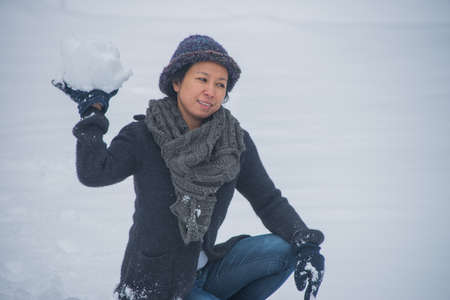 Asian woman in hat holding piece of snow in her hand