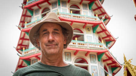 senior citizen with green shirt and hat standing in front of Buddhist templeの写真素材