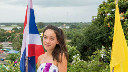 Smiling teen standing in front of Thai flag with town in the background