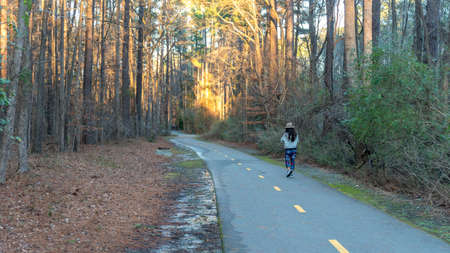 woman with hat  walking down empty bath in woods with puddles on bike path
