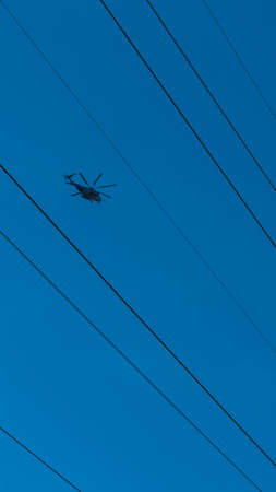 Helicopter flying between high tension wires with a clear dark blue sky