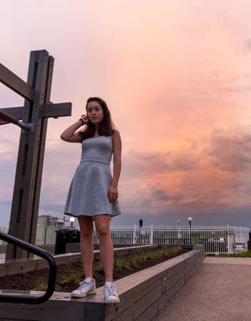 Teen girl in dress standing on bollard in front of Potomac River with mobile phone in her handの写真素材