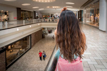 Back of woman with long brown hair at mall with pink sweater around her waist