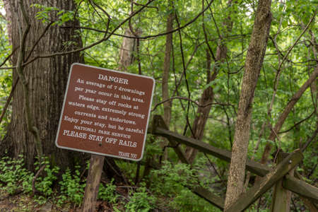 Brown and white sign warning of drownings and to be careful in forest at Great Falls National Parkの写真素材