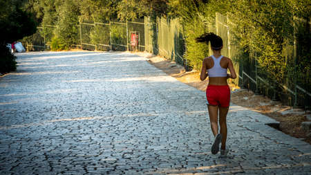 Teen in red shorts and white tanktop jogging on cobblestone road in Athens Greece