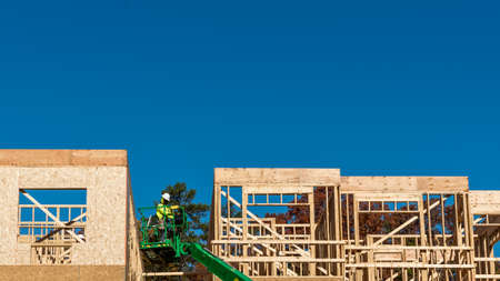 Construction worker elevated in hydraulic platform working on building with blue sky in background