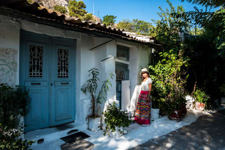 Asian woman in white t-shirt in Athens in white hat and sarong standing in front of house in old section of Plakaの写真素材