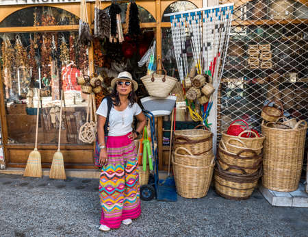 Asian woman in white t-shirt  in Athens in white hat and sarong standing in front of shop with baskets and woven goods in Psiriの写真素材