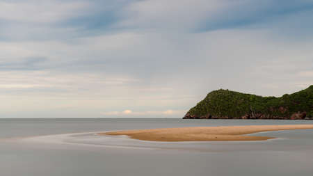 Sand bar sticking our of water at low tide with mountain behind it in Prak Nam Pran Thailand