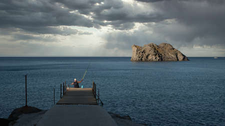 Fisherman sitting on a delapidated dock on a stormy day with island in the background on the island...