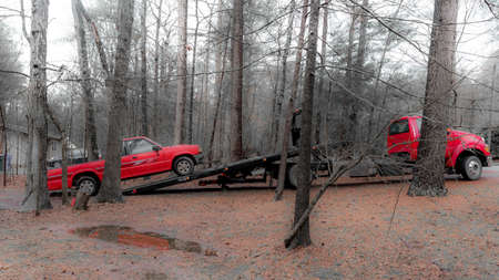 Red pickup truck being loaded on red tilt bed tow truck to be hauled away on winter day in North Carolinaの写真素材