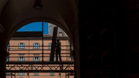 Silhouette of workman standing on scaffold in archway in Bologna Italyの写真素材