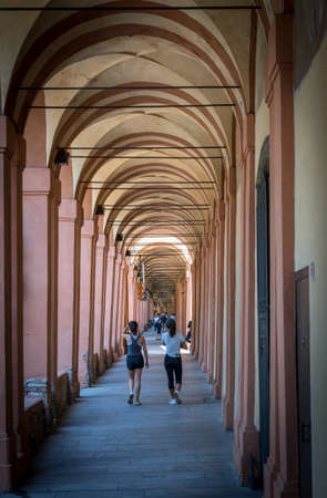 Mother in black hat and daughter walking down promanade in sneakers and shorts and pants in Bologna Italyの写真素材