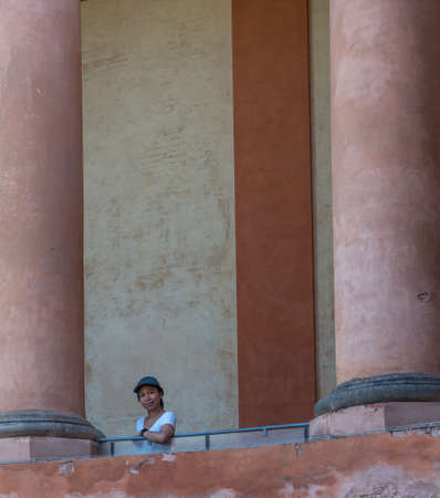 Asian woman in tshirt and hat standing on balcony between large columns in Bologna Italyの写真素材