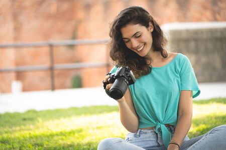 Photographer girl sitting on the grass looking at the camera screen, smiling
