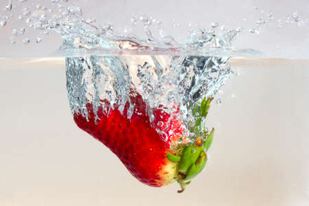Water splashing on a strawberry against a white backgroundの写真素材
