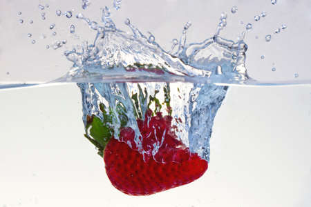 Water splashing on a strawberry against a white backgroundの写真素材