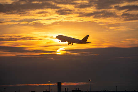 Side silhouette of airplane flying take off over a city during sunsetの写真素材
