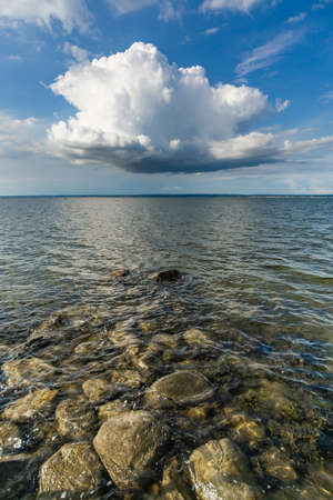 Large cloud floating over the sea, and small rocks in the shoreの写真素材