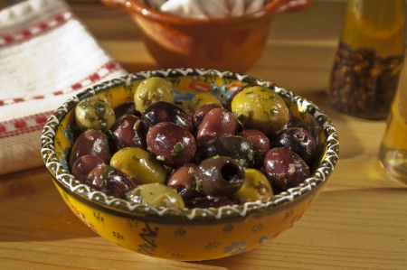Bowl of delicious black and green olives with garlic and two bottles of oil in the backgroundの写真素材
