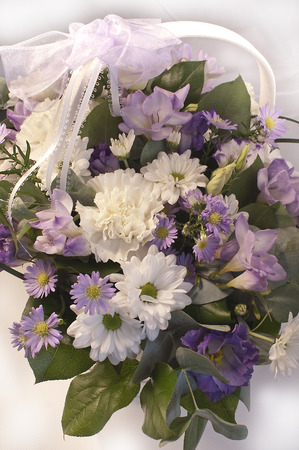 Beautiful bouquet of white, lilac and purple flowers in a basket with a lace ribbonの写真素材
