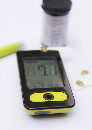 Blood glucose monitor with a lancet, some test strips and a test strips tub in the background, shalow depth of fieldの写真素材